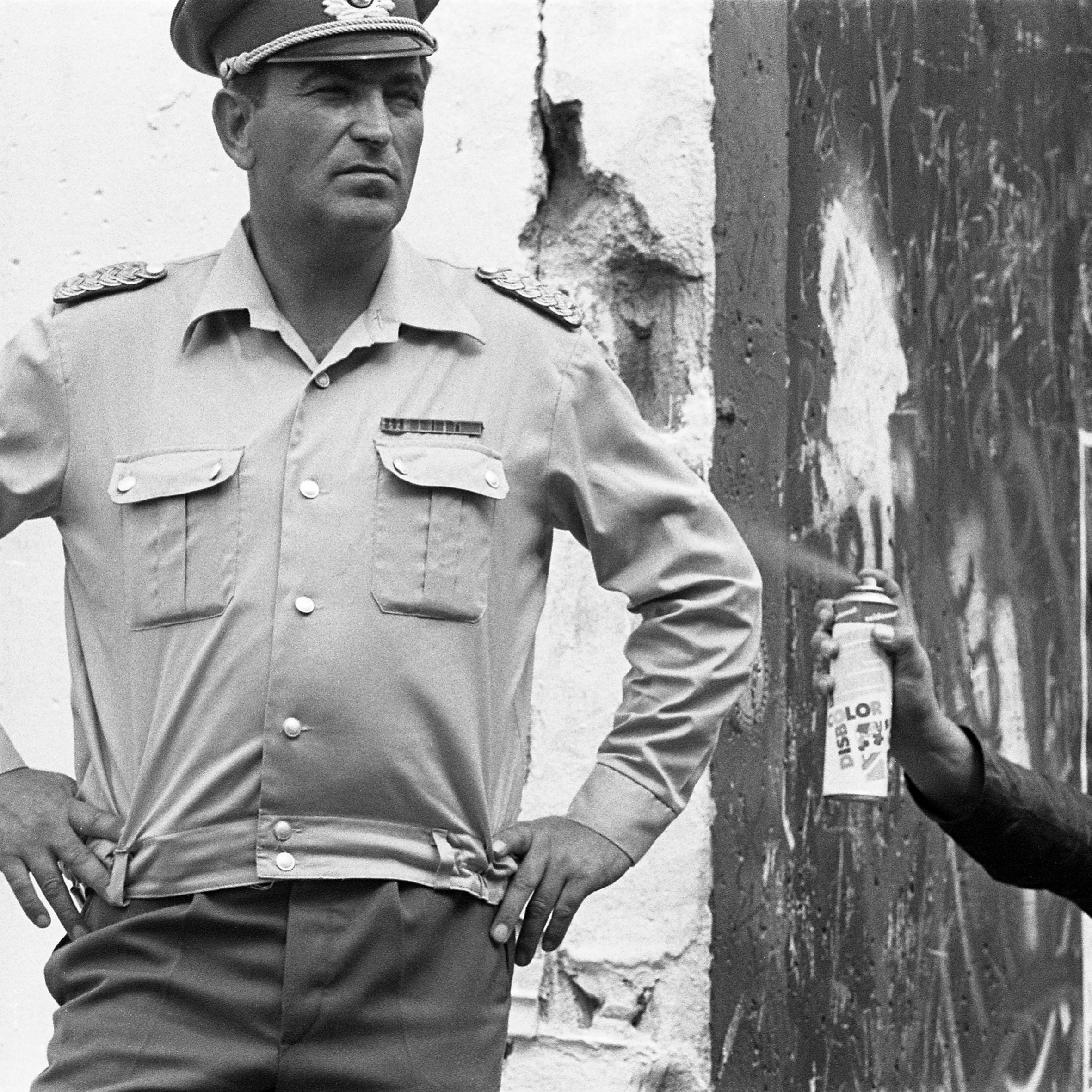 Un hombre uniformado fuma junto a un muro desconchado, fotografía callejera en blanco y negro de David Hornback