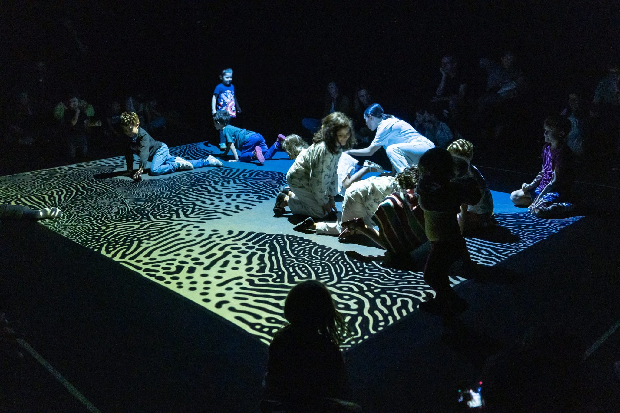 Varios niños y niñas con las bailarinas sobre la alfombra digital de Gesto, de Taiat Dansa