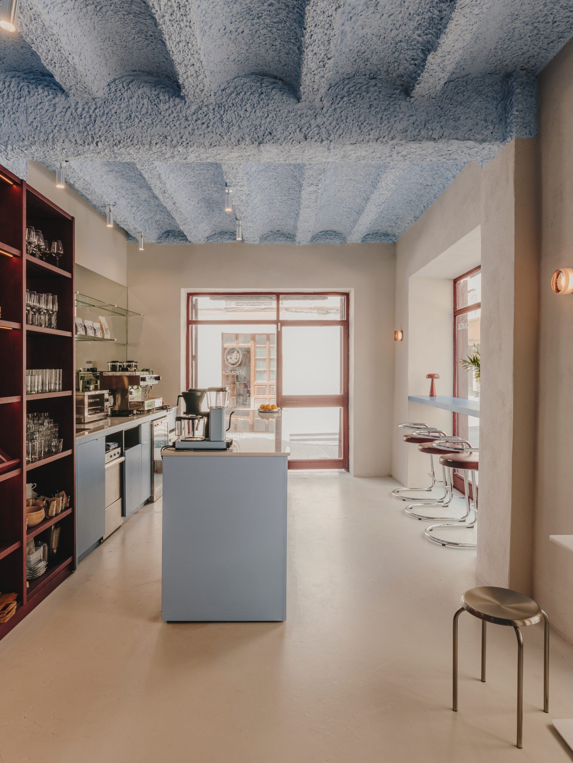 Interior de Chiquita: barra, estantería burdeos y techo azul junto a la entrada.